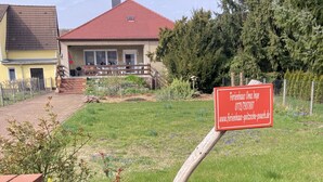 A residential property with a red-roofed house, a wooden fence, and a signboard with contact information. - Ferienhaus Oma Inge Zwischen Goitzsche und Muldestausee Haustierfreundlich ! (Muldestausee)