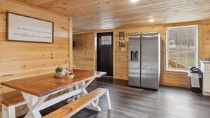 A wooden interior with a wooden table and benches, a refrigerator, and a window with a view. - Majestic Valley Retreat 2 Bedroom Cabin by RedAwning (Sevierville)