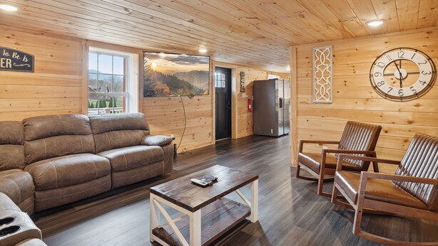 A wooden interior with a sofa, chairs, a coffee table, a clock, and a window with a view. - Majestic Valley Retreat 2 Bedroom Cabin by RedAwning (Sevierville)