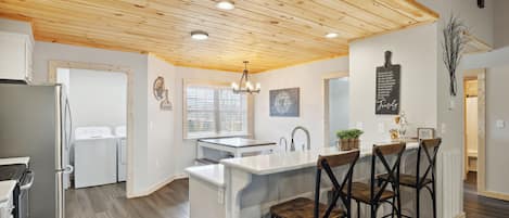 A modern kitchen with wooden ceiling, stainless steel appliances, and a central island with bar stools.