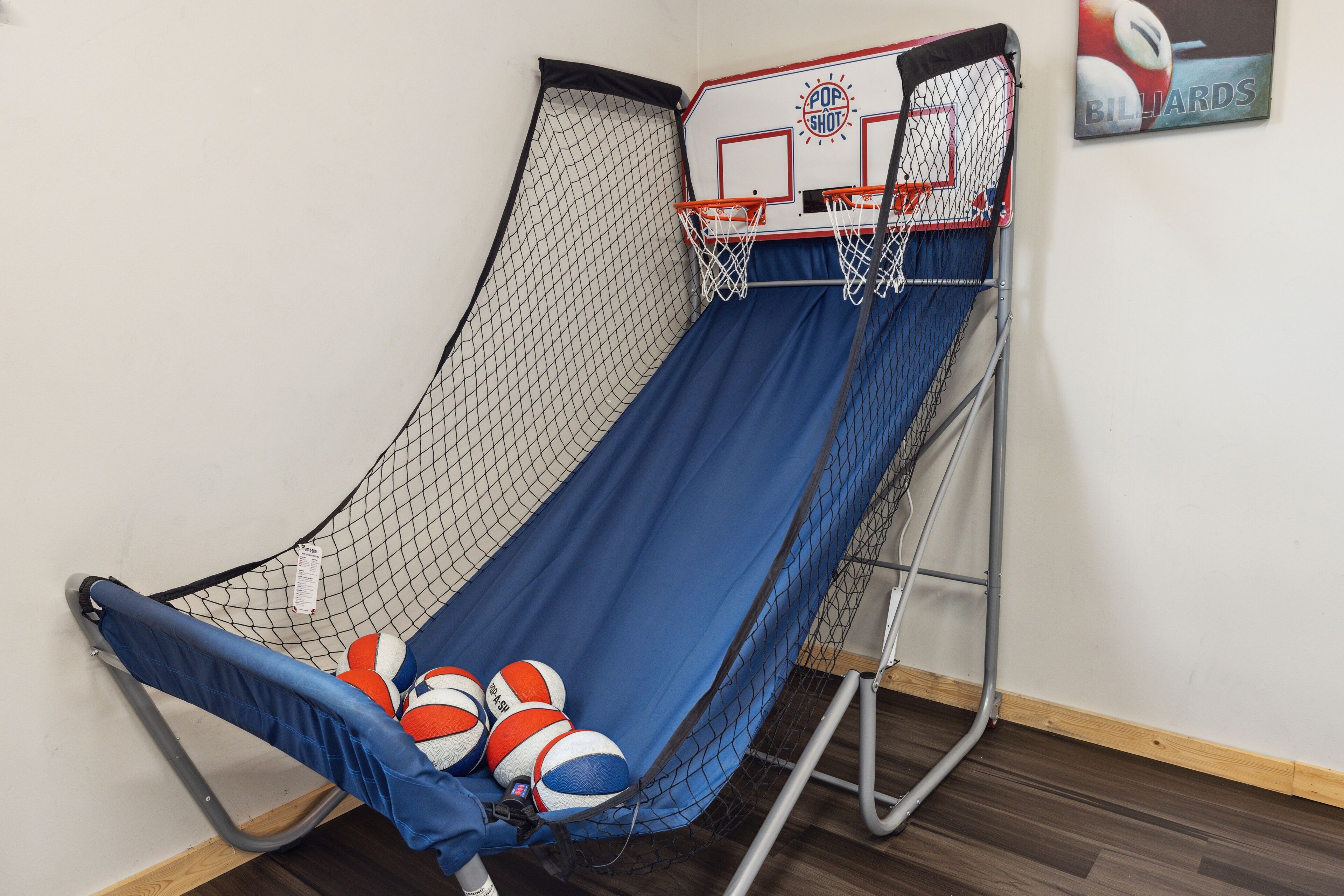 A small indoor basketball court with a net, two basketball hoops, and a blue padded floor.