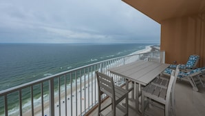 A balcony with a view of the ocean, a table, and two lounge chairs.