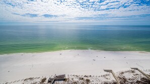 Ein Strand mit einer Holzpromenade, die zum Wasser führt, strahlend blauem Himmel und ruhiger See.