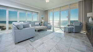 Amplia sala de estar con un gran ventanal con vistas a la playa, un ventilador de techo y suelo de baldosas.