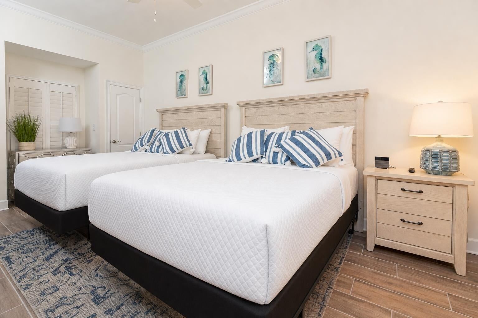 A hotel room with two beds, a nightstand, a lamp, and wall art.