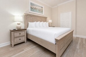 A bedroom with a bed, nightstands, a painting, and a window with shutters. - Phoenix Gulf Towers 602 2 Bedroom Condo (Orange Beach)