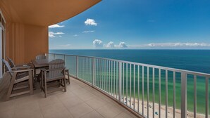 A balcony with a view of the ocean, a table, and chairs. - Phoenix Gulf Towers 2003 3 Bedroom Condo (Orange Beach)