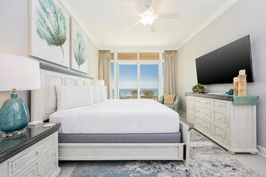 A bedroom with a bed, a TV, a ceiling fan, a dresser, and a view of the ocean. - Phoenix Gulf Towers 2401 4 Bedroom Condo (Orange Beach)