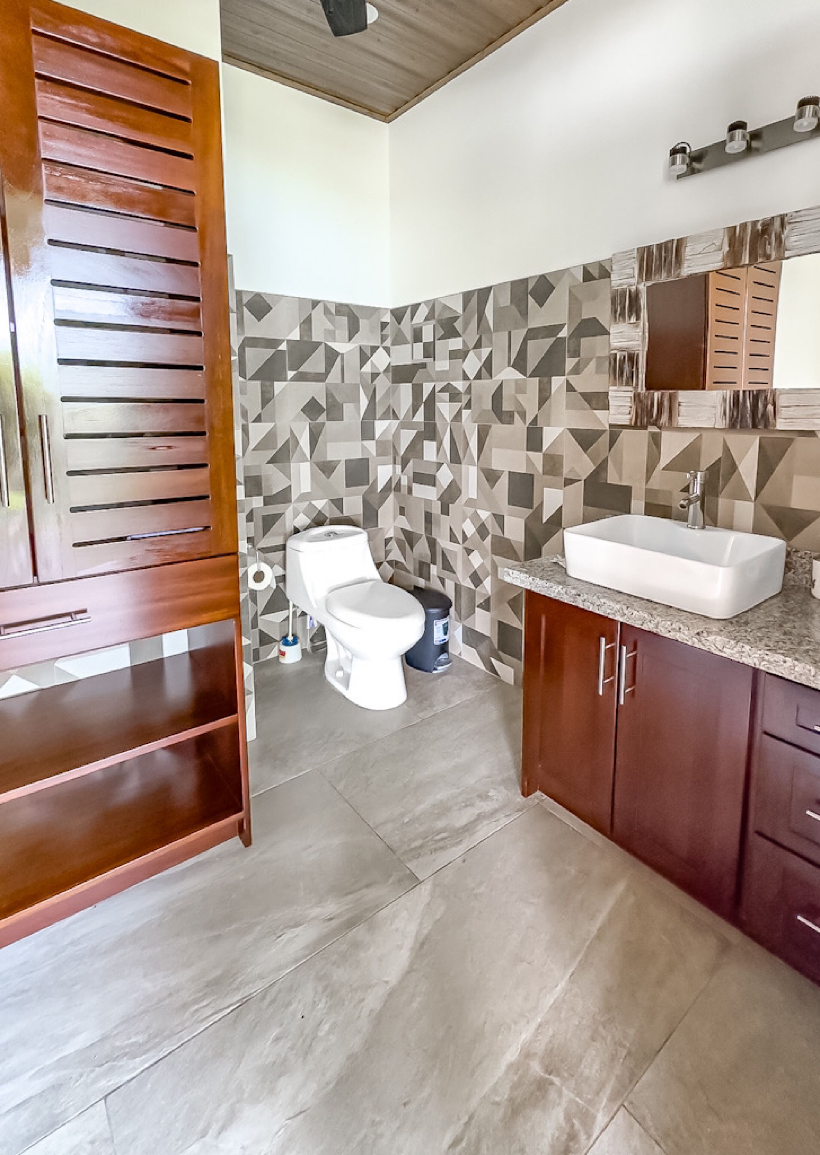 A bathroom with a toilet, sink, and wooden cabinets.