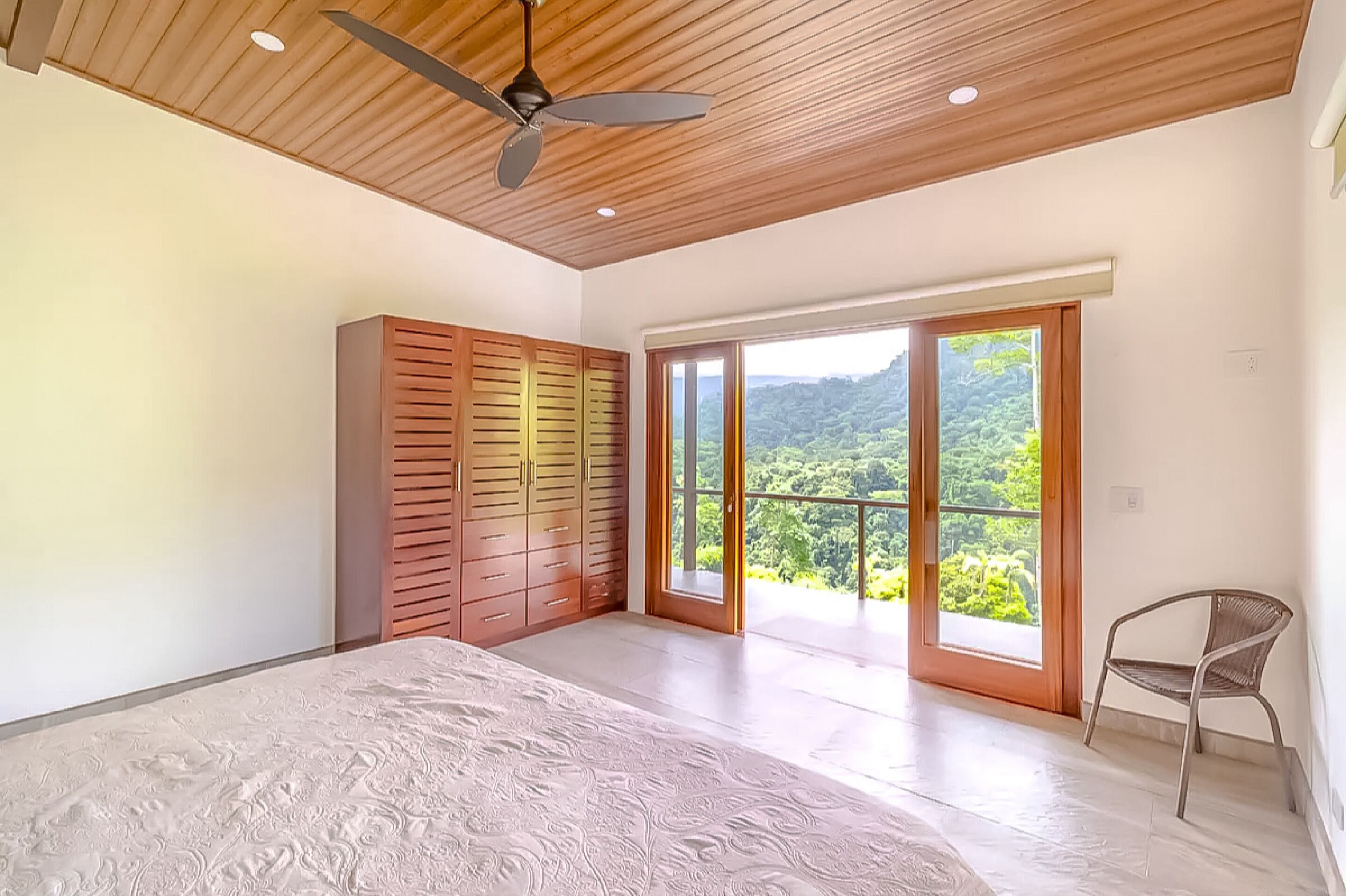 Un dormitorio con cama, armario, ventilador de techo y balcón con vistas a zonas verdes.