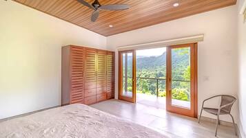 Un dormitorio con cama, armario, ventilador de techo y balcón con vistas a zonas verdes.