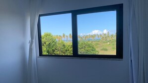 Une chambre avec un lit, une fenêtre donnant sur une plage et des palmiers.