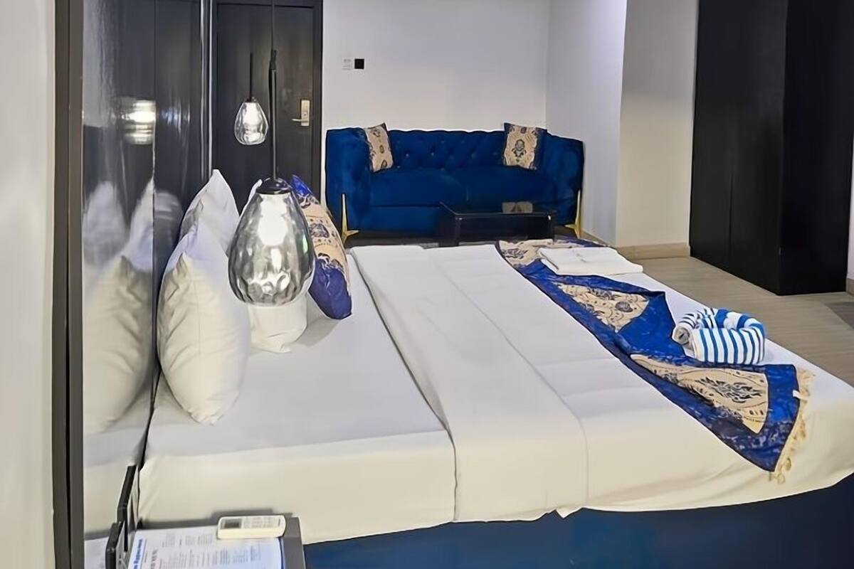 A modern hotel room with a large bed, a blue sofa, a wardrobe, and a mirror.