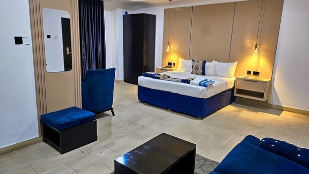 A modern hotel room with a large bed, a sofa, a coffee table, and a desk with a lamp. - Water Ripples Hotel (Lekki)