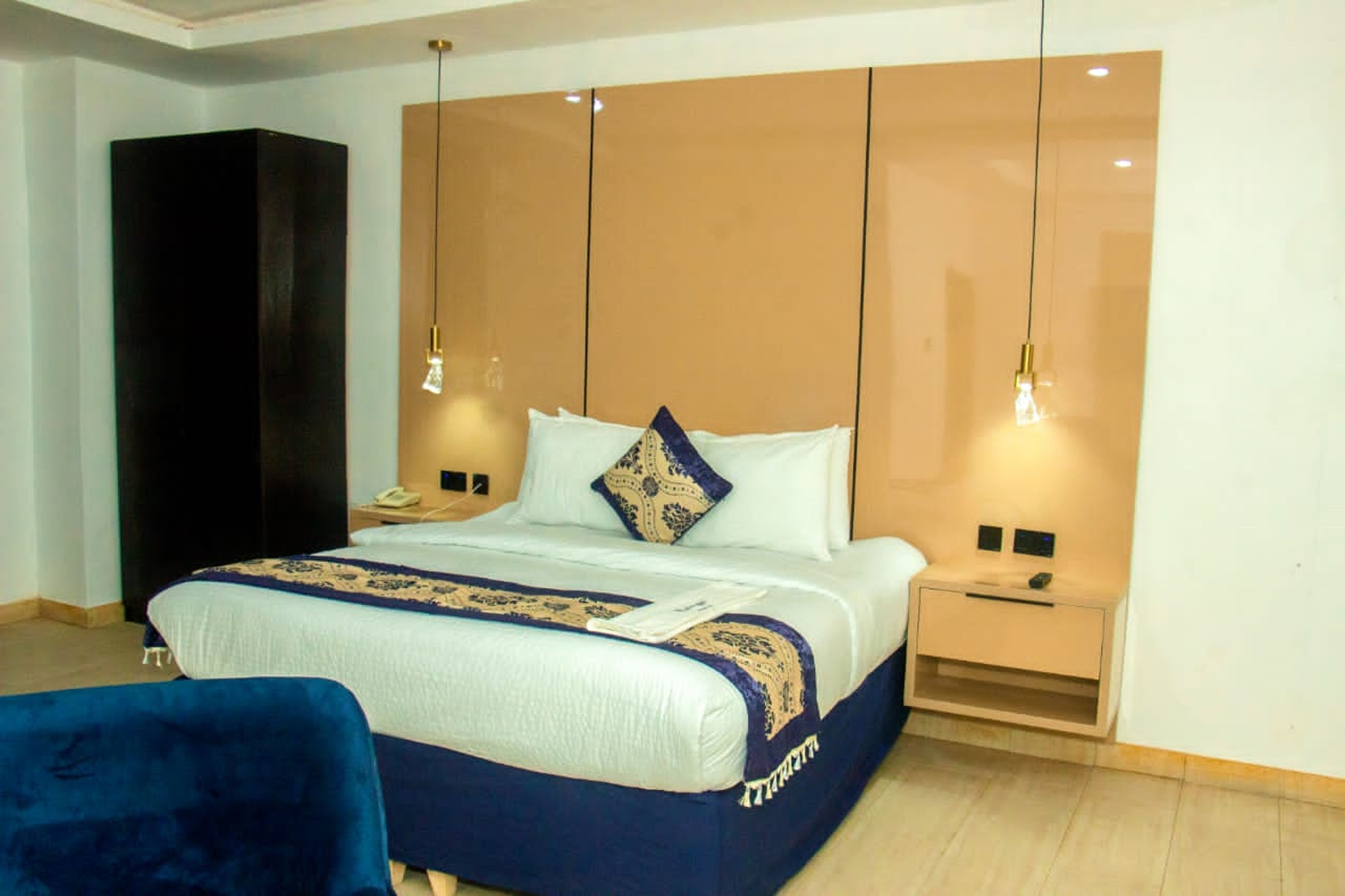 A modern hotel room with a large bed, bedside tables, and a wardrobe.