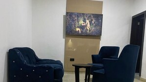 A modern living room with two dark blue sofas and a small table, a large abstract painting on the wall, and a wooden floor. - Water Ripples Hotel (Lekki)