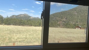 Uma janela com vista para um campo gramado, árvores e montanhas.