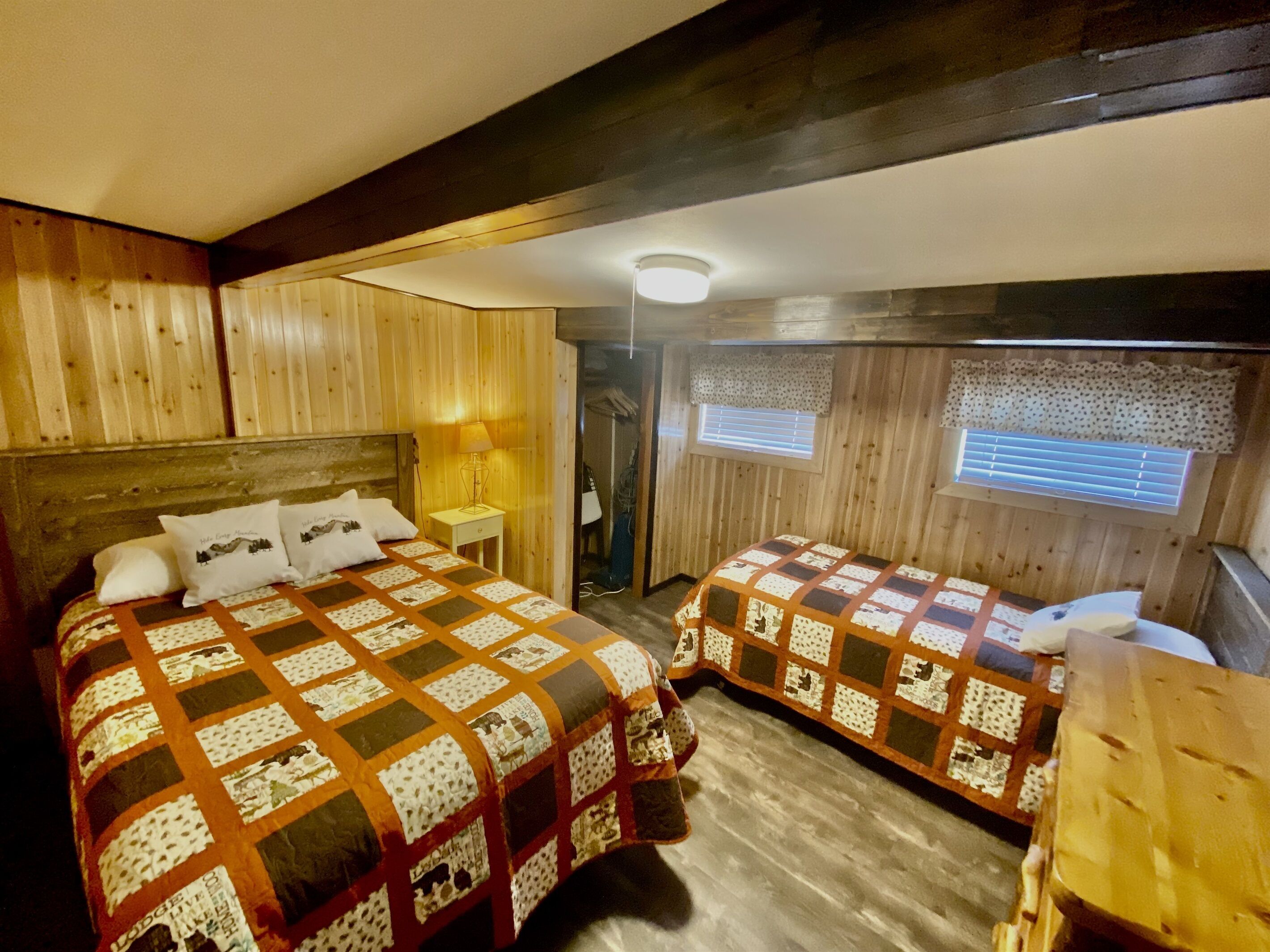 Una habitación acogedora con dos camas, paredes de madera, un ventilador de techo y una ventana con persianas.