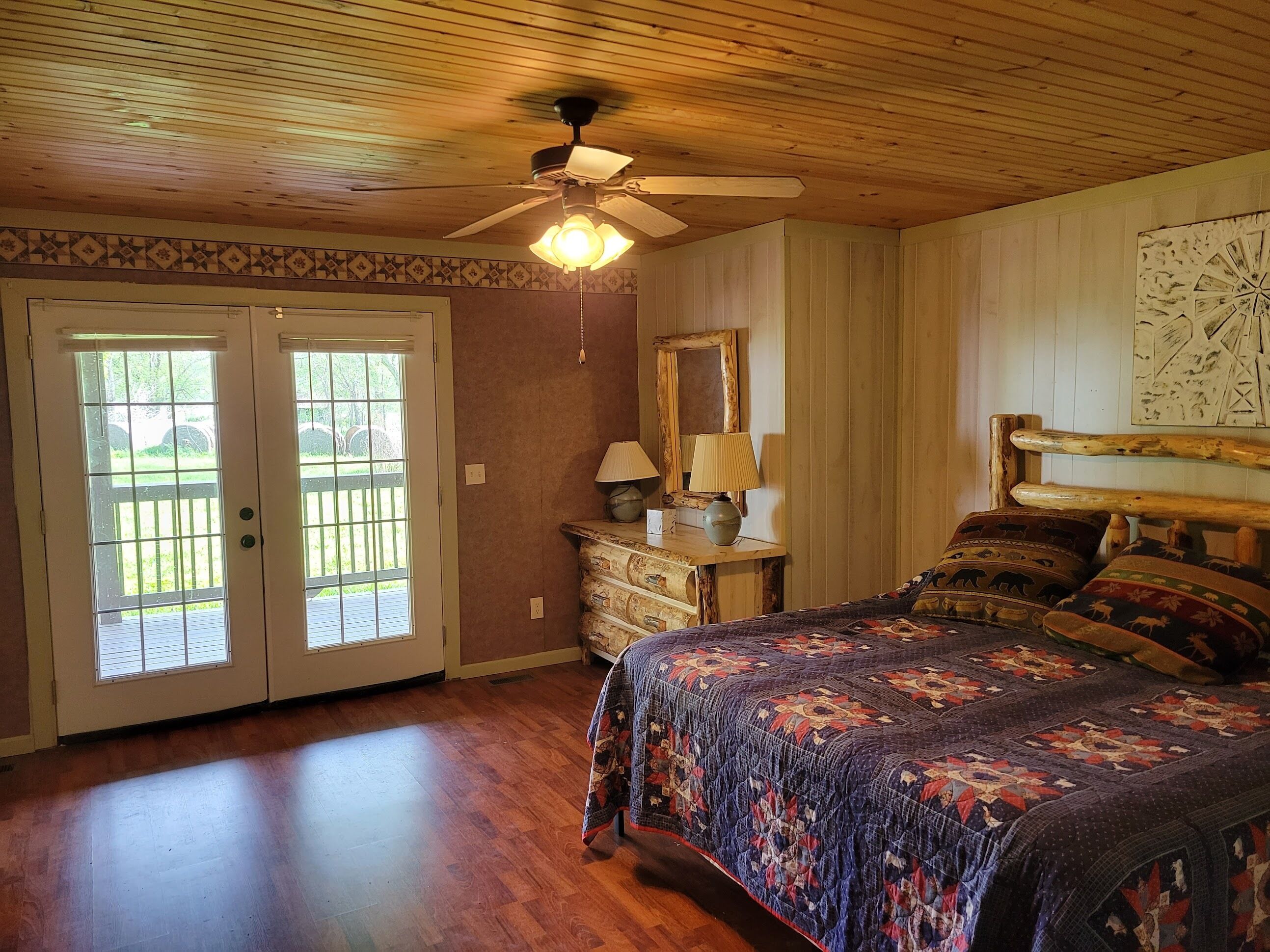 A bedroom with a wooden ceiling, a ceiling fan, a bed with patterned bedding, a dresser, and a mirror.