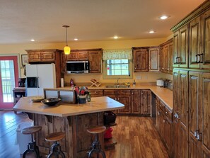 Una cocina amplia con armarios de madera, una isla grande con taburetes, un microondas y un refrigerador.