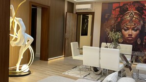A modern living room with a grey sofa, a glass coffee table, and a dining area with white chairs. - Vika Luxury 3 Bedroom Serviced Apartment (Abuja)