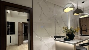 A modern kitchen with marble backsplash, pendant lighting, and a central island with a black countertop and gold accents. - Vika Luxury 3 Bedroom Serviced Apartment (Abuja)