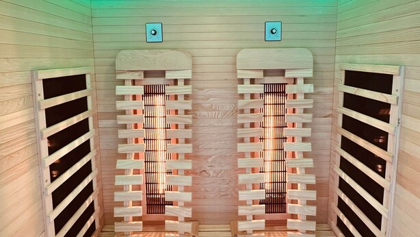 Un sauna avec des murs et des bancs en bois, un plafond doté d’un système de ventilation et une bande lumineuse verte.