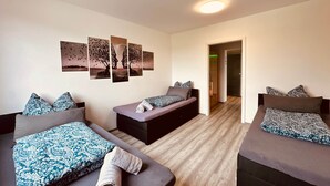 Une chambre d’hôtel avec deux lits, un canapé-lit, un mur décoré d’œuvres d’art et un couloir menant à une autre pièce.