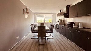 Une cuisine moderne avec des meubles de couleur sombre, une table à manger avec des chaises et une grande fenêtre qui laisse entrer la lumière naturelle.