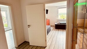 Un couloir avec un plancher en bois, une porte blanche et une vitrine illuminée d’une lumière verte.