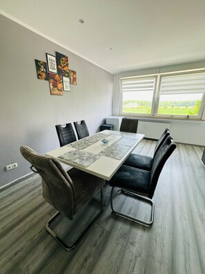 Ein moderner Essbereich mit einem rechteckigen Tisch, schwarzen Polsterstühlen und Blick auf eine grüne Landschaft durch große Fenster.