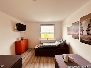 Una habitación pequeña con cama, televisor, cómoda y ventana con vista a un campo.
