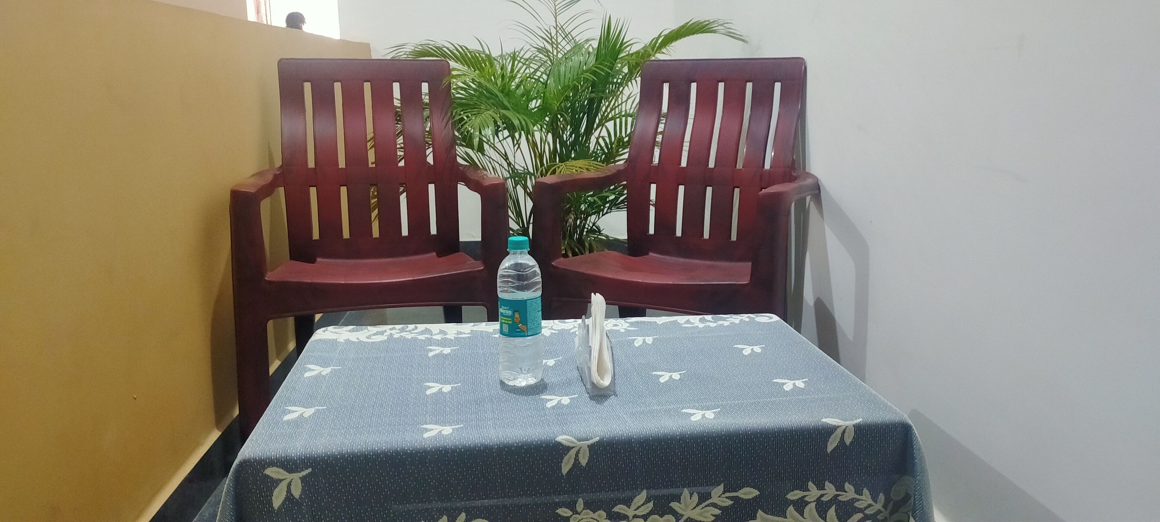A small table with a floral tablecloth, two wooden chairs, a water bottle, and a napkin on the table.