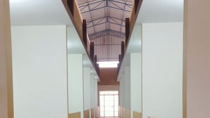 A long, narrow hallway with tiled floors and white walls, leading to a bright exit. - Hotel PSR Executive Rooms by VINHOTELS (Bengaluru)