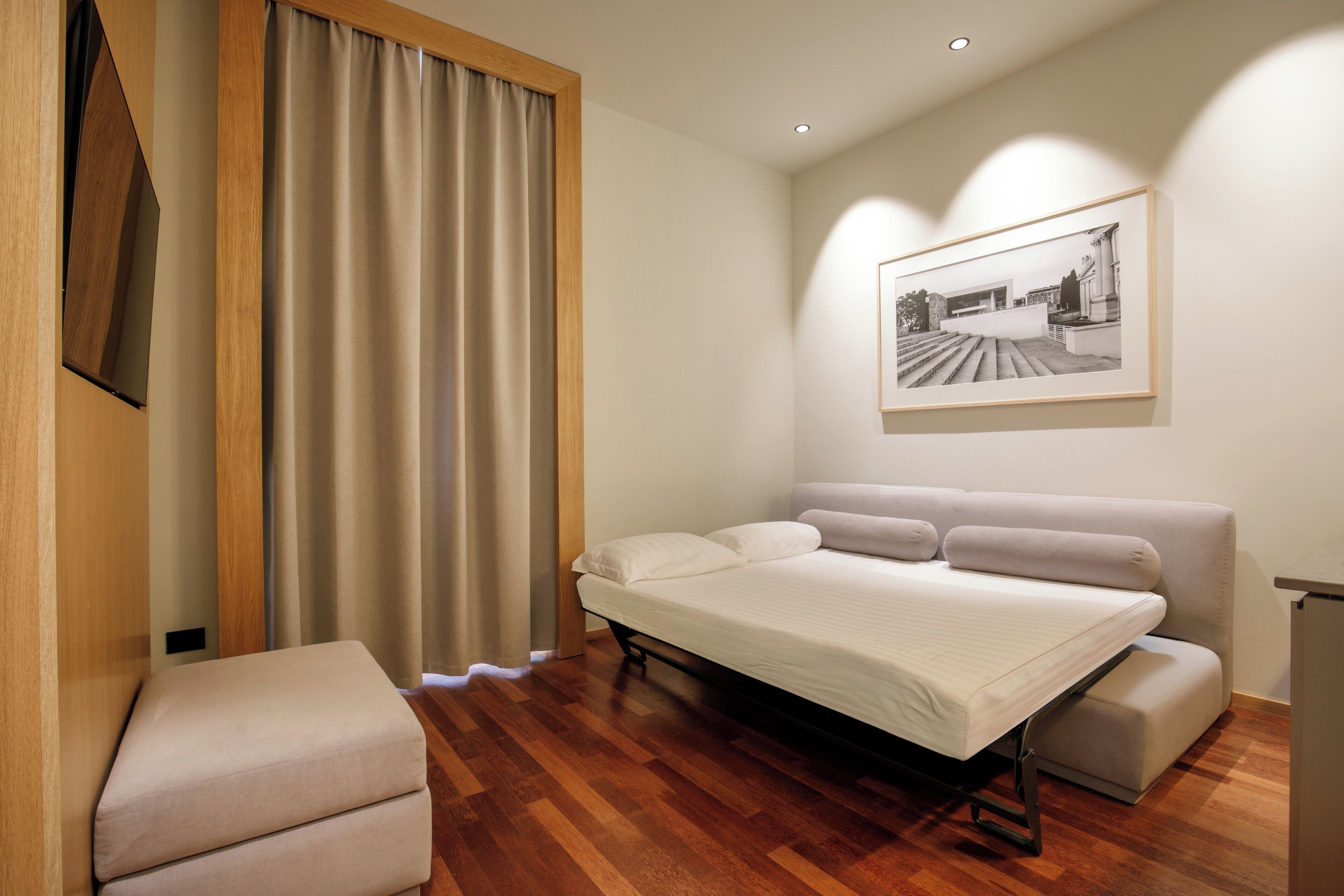 A modern bedroom with a bed, a small seating area, and a framed picture on the wall.