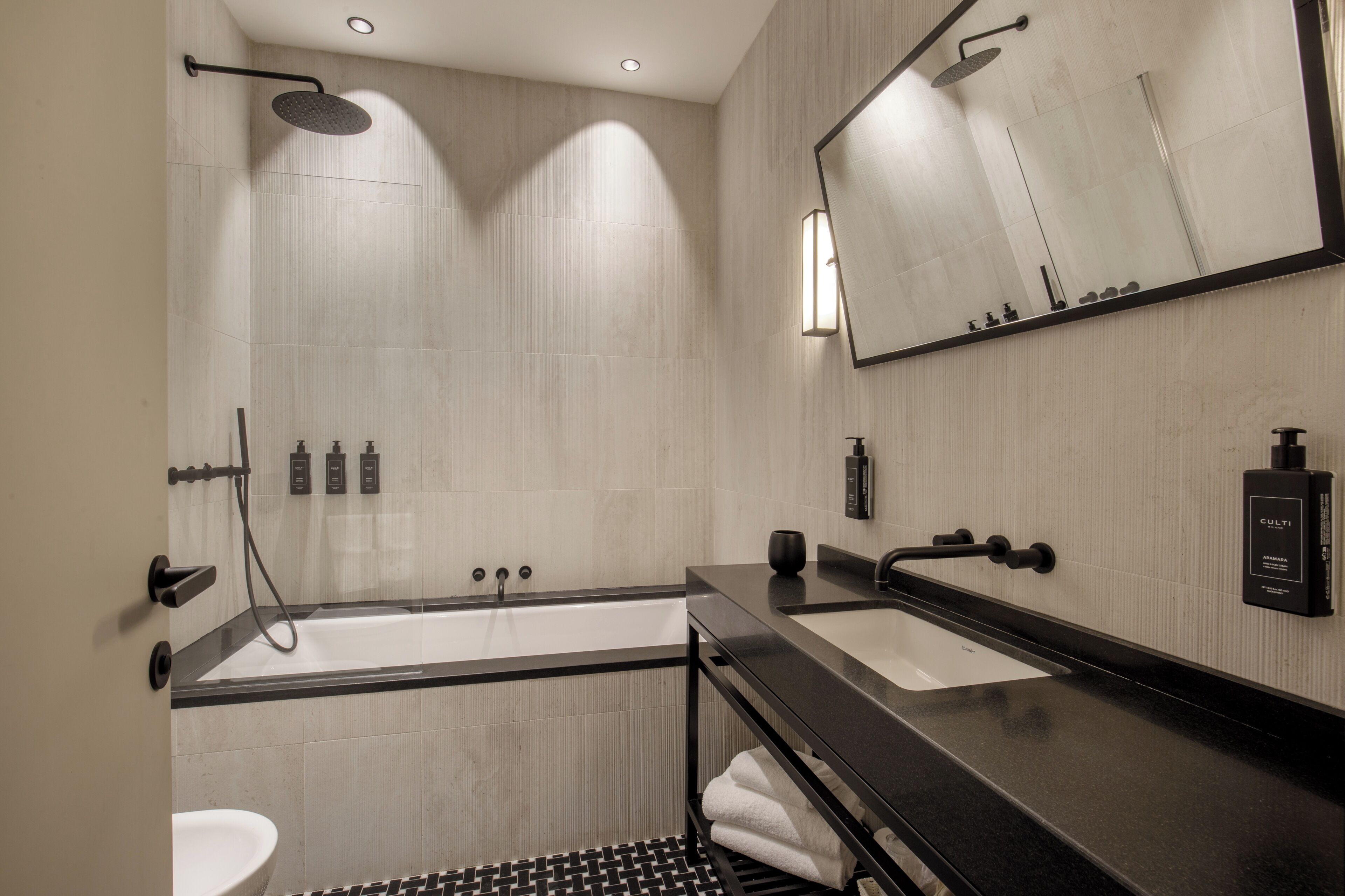 A modern bathroom with a bathtub, two sinks, a large mirror, and a shower.
