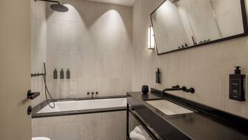 A modern bathroom with a bathtub, two sinks, a large mirror, and a shower.