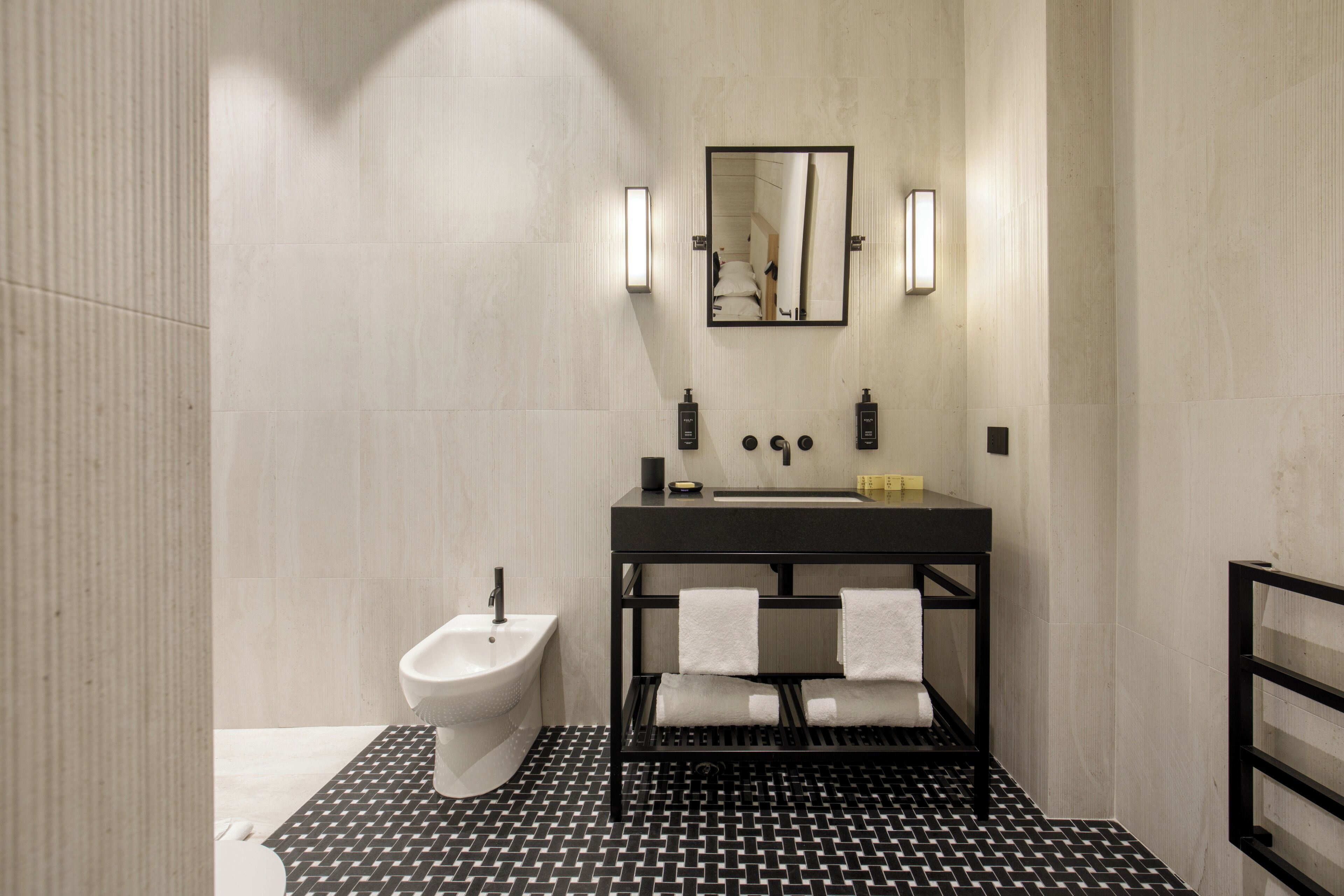 A modern bathroom with a black and white tiled floor, a black vanity with a mirror, and a bidet.