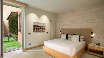 A modern bedroom with a large bed, a wooden headboard, a nightstand, and a view of a green garden through a sliding door.