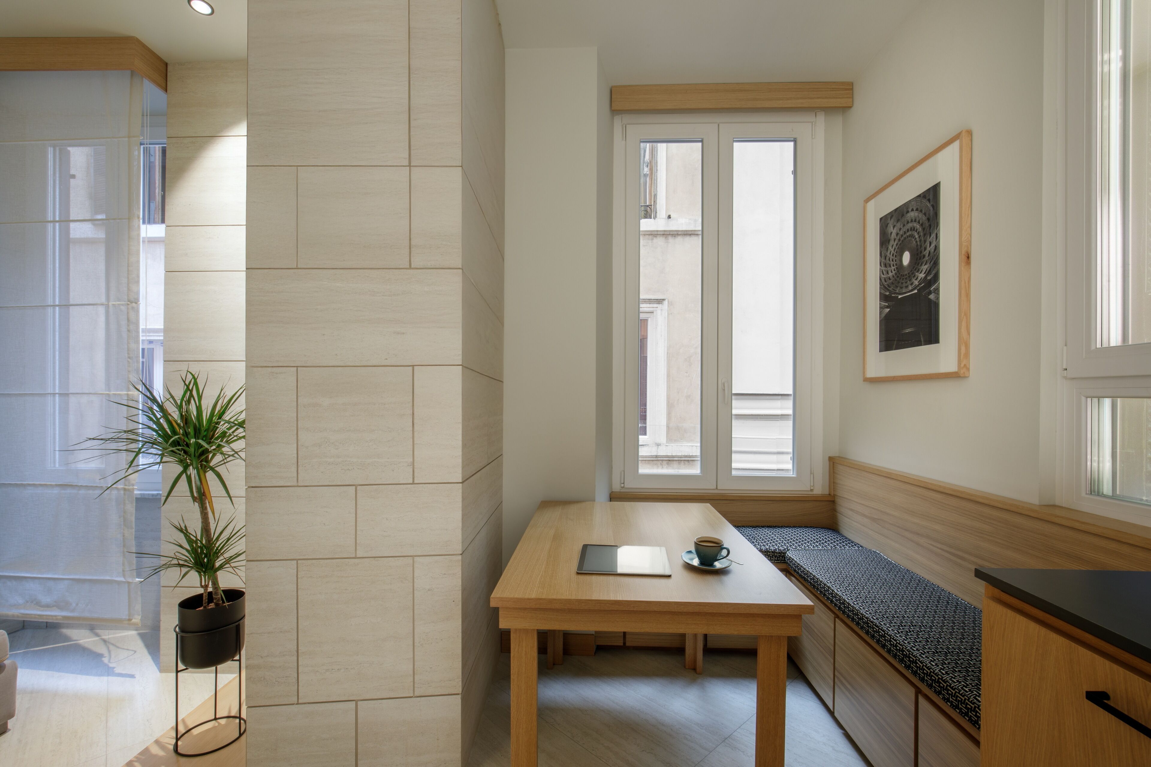 A modern kitchen with a wooden table, a bench, and a potted plant.