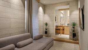 A modern living room with a sofa, a dining area, and a kitchen visible through an open doorway. - Ripetta Luxury Apartments (Rome)