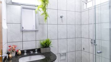 Uma casa de banho moderna com lavatório de mármore, cabine de duche em vidro e uma planta em vaso.