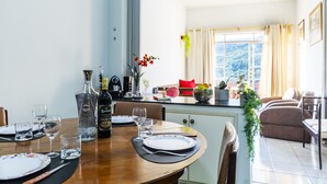 A dining area with a wooden table set for four, a bottle of liquor, and a vase with flowers. - Apartamento aconchegante. Vista incrível (Águas de Lindóia)
