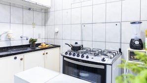 A modern kitchen with white cabinets, a black countertop, a gas stove, and a blender on the counter. - Apartamento aconchegante. Vista incrível (Águas de Lindóia)