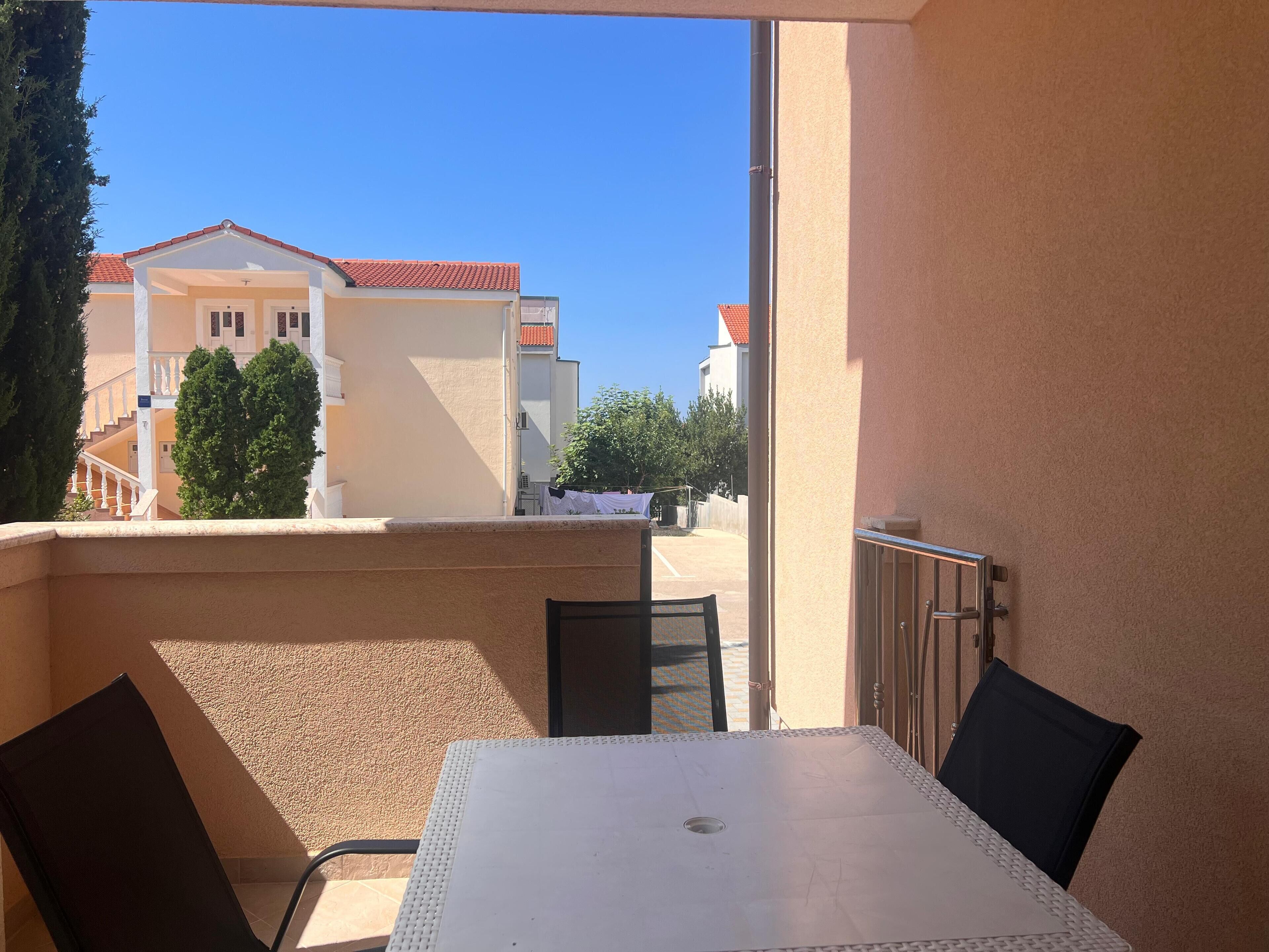 A balcony with a table and chairs, overlooking a residential area with houses and trees.