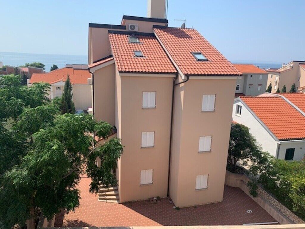 Un edificio de varios pisos con techo de tejas rojas, paredes exteriores color beige y varias ventanas.