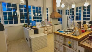 A spacious kitchen with white cabinetry, a central island, and a large window overlooking a blue sky. - Casa Iracema da Serra (Vale do Paquequer)