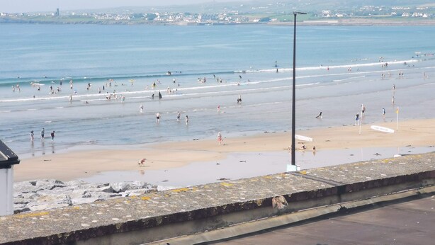 Una playa con gente nadando y caminando por la orilla, una torre de salvavidas y una vista despejada del mar.