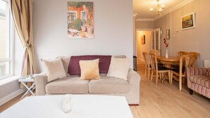 Una sala de estar con un sofá color beige, una mesa de comedor con sillas y un cuadro en la pared.