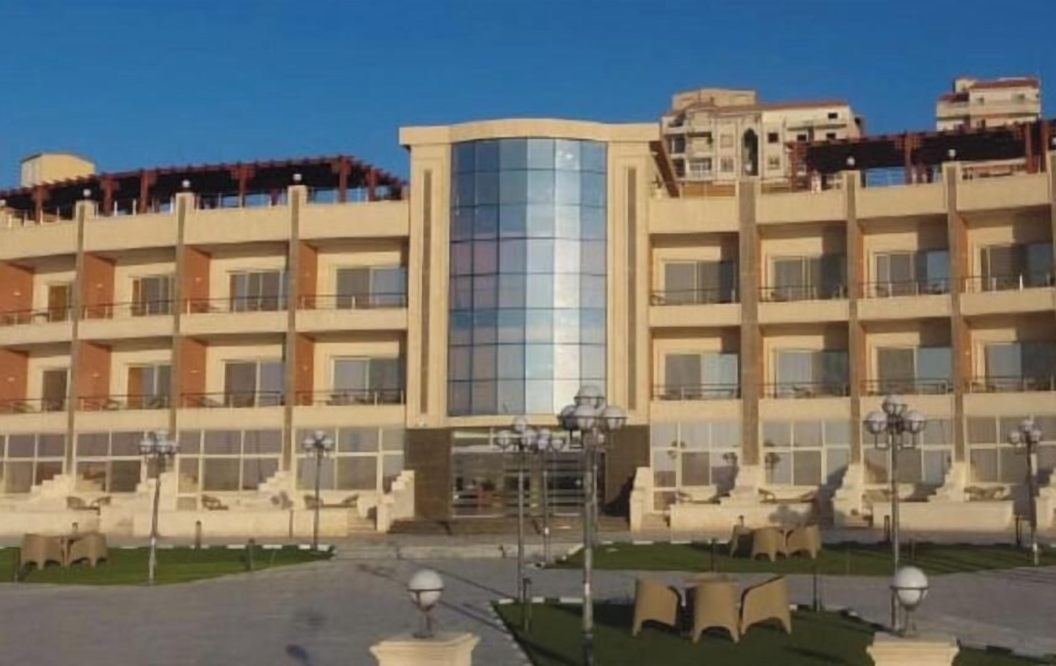 A multi-story hotel with a central glass facade, outdoor seating area, and a well-maintained courtyard.